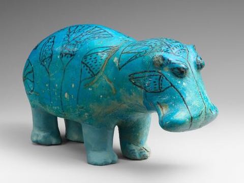 A small turquoise faience hippopotamus figure, its flank painted with dark lotus motifs, photographed against a plain studio background.